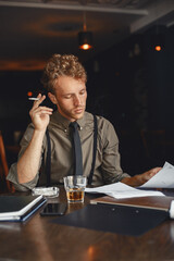 A man with bristles sits and smokes a cigarette.
