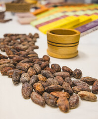 Presentation of dried cocoa beans and a wooden cup for manually grinding cocoa. With chocolate boxes in the background.
