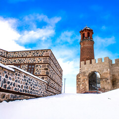 Erzurum Castle and stone houses covered in snow under a clear blue sky.