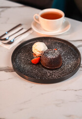Chocolate Volcano Cake with Ice Cream and Strawberry on Black Plate with Tea on Marble Table