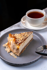 Baklava Cheesecake Slice with Walnuts and Crispy Filo on Plate with Tea on Marble Table