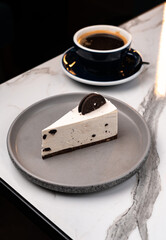 Cookies and Cream Cheesecake Slice on Plate with Black Coffee on Marble Table