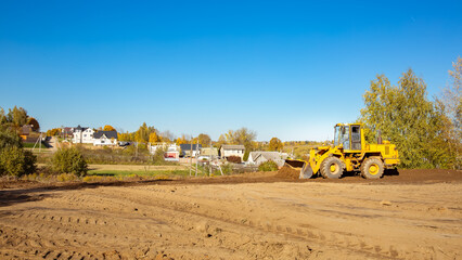 Yellow bulldozer at a construction site. Big wheel excavator leveling and clearing the land plot side view. Moving earthworks soil. Copy space. Building area. Special transport. High quality photo. © Hanna