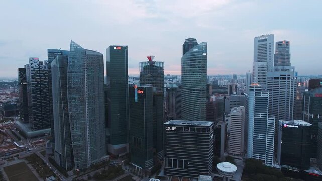 Aerial view of Singapore's central business district with skyscrapers, including the ANZ and UBS towers, under a soft blue sky during sunset.