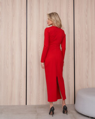 Blonde woman in an elegant red dress with long sleeves and slit, standing in profile, wearing black...
