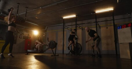 Four athletic people doing different intense exercises during strength training with timer in modern comfortable fitness room. Guys and girls in group strength training