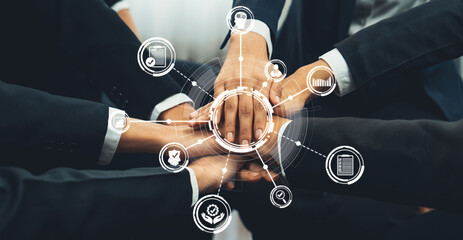 A diverse business team stacks their hands together, symbolizing unity and partnership. Surrounding...