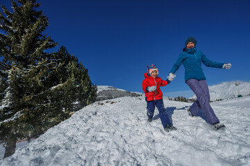 Mother with boy kid running down the slop on winter vacations