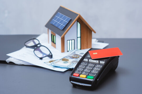 Payment terminal for credit card payment, US dollars and solar powered house model. Concept of property payment and real estate transactions for green housing.