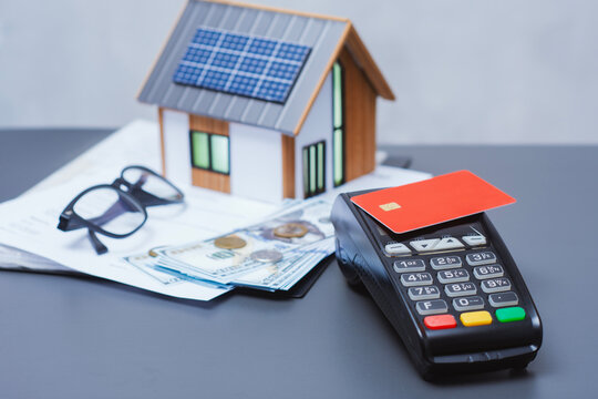 Payment terminal for credit card payment, US dollars and solar powered house model. Concept of property payment and real estate transactions for green housing.