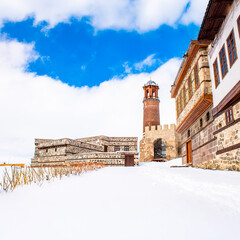 Snowy Erzurum Castle and historic Ottoman houses under a bright winter sky.