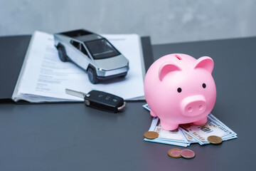 Pink piggy bank on a US dollar bills with coins, car key and electric vehicle on contract papers. Concept for saving money for buying an electric car, car loan, financial planning.