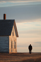 solitary figure stands in front of old weathered house as daylight saving time ends