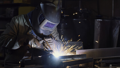 A welder wearing protective gear skillfully joins metal pieces, creating bright sparks in an industrial workshop setting.