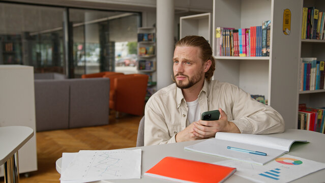 Caucasian student man with mobile phone at table in class lesson in classroom using mobile phone chatting online male guy studying problem gadget addiction smartphone game dependence education study