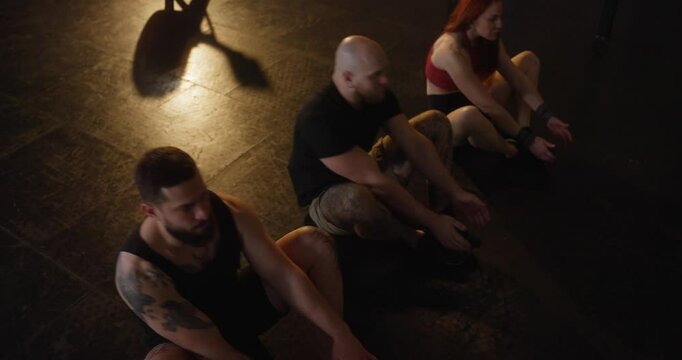 Top view group of athletic people doing abdominal exercises and crunches in a row on black floor in modern fitness room with yellow lighting