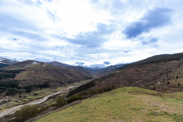 Breathtaking valley landscape with snow-capped mountains and winding river under cloudy sky