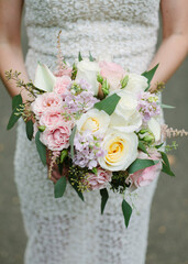 Bridal bouquet of mixed flowers featuring roses, lilies, and greenery held by a bride in a lace...