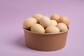 Brown eggs in kraft paper bowl on purple background