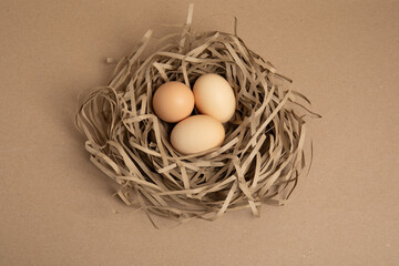 Three brown eggs in paper nest on brown background – top view