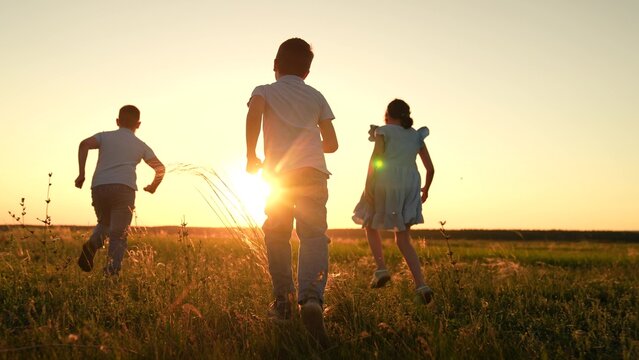 Active running of happy children, running on grass in field in summer in sun. Children team running on grassy lawn. Children playing in spring park. Child play in nature. Happy family in park concept