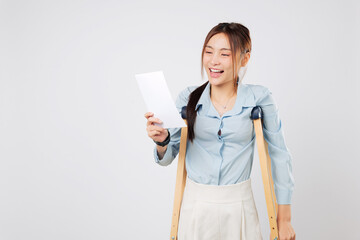 Cheerful woman with leg injury holds bill payment paper and smiles, using crutches for support and crutches to balance during recovery. isolated studio white background