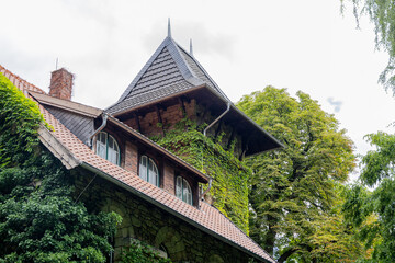 Historic building with ivy-covered walls and a steep roof, surrounded by lush greenery, showcasing architectural beauty and nature's embrace
