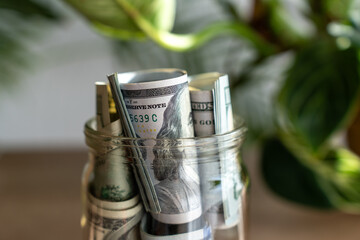 Close-up of tightly rolled hundred dollar bills secured with rubber band on blurred wooden...