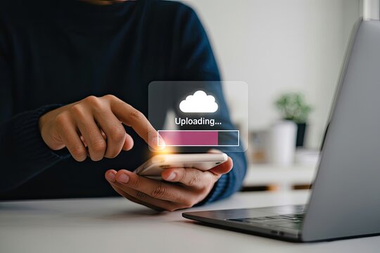 Person uses smartphone to upload data to the cloud with progress bar visible on screen next to laptop