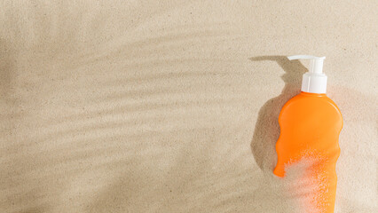 Top view of orange bottle of sunscreen on white clean sand in the shade of palm tree. Summer beach holiday, UV protection concept.
