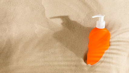 Summer vacation, UV protection concept. Orange sunscreen on the sand in the shade of a palm tree.
