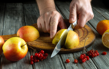 Hands are busy cutting fresh apples on a wooden board. The setting includes various fruits like...