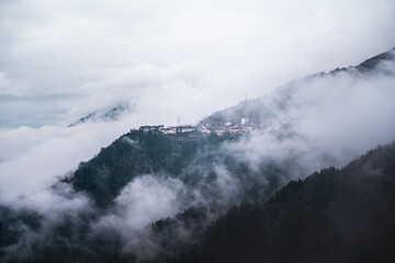 Panoramic horizontal view of small Italian mountain village enveloped in fog and clouds during cold autumn season