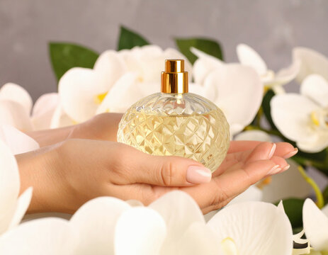 A woman's hands gently cradle a perfume bottle surrounded by white orchids, capturing elegance and luxury in a fragrant setting.