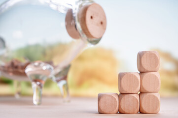 Wooden blocks near transparent piggy bank alongside coins representing financial planning, investment, and savings with a blurred neutral backdrop promoting sustainable themes
