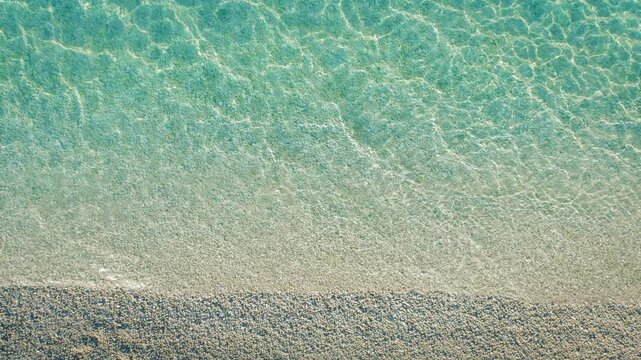 Detailed aerial view of crystal-clear shallow waters gently lapping a pristine white pebbled shore in Kefalonia Greece in summer