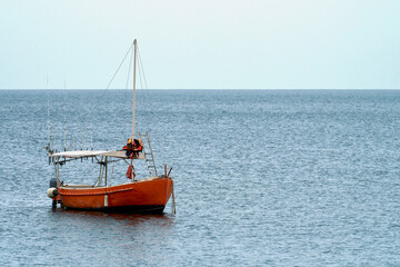 Sea fishing. A lonely red boat with many different fishing rods on board is anchored in the middle of the sea.