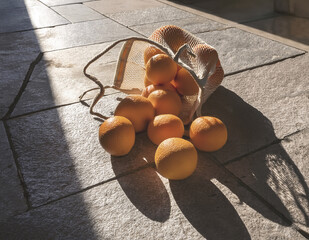 A group of oranges spilled from a market bag onto a sunlit stone floor with rich shadows