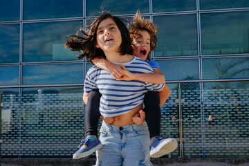 girl in striped t-shirt and jeans jumping with smaller girl carried on her back
