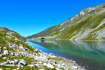 Shore of Dösner alpine lake with a reflection of the mountains in the water in High Tauern, Carinthia, Austria