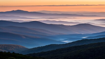 Fototapeta premium Layered mountain peaks shrouded in mist under a warm sunrise sky