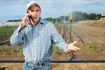 Portrait of caucasian man farmer standing on vegetable field and talking on phone.