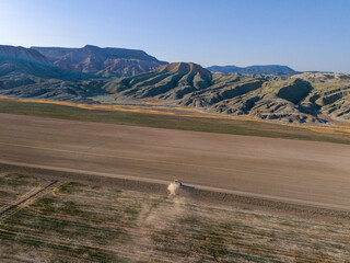 Nallıhan Aerial View of a Dusty Field with Dramatic Mountains. High-angle, expansive shot of a dry, flat field, likely farmland, with a light dusting of dust rising from a vehicle or machine traversin