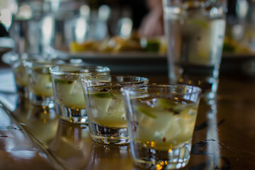 Close-up of a series of shot glasses filled with a clear liquid, ice, and lime slices on a wood surface, creating a refreshing vibe.