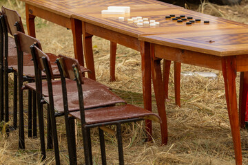 Outdoor wooden table with a checkerboard and checkers, accompanied by chairs on dry grass, setting the scene for a relaxed game or social gathering in nature