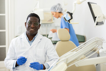 Confident qualified african american dentist posing in modern dental clinic office, looking at...