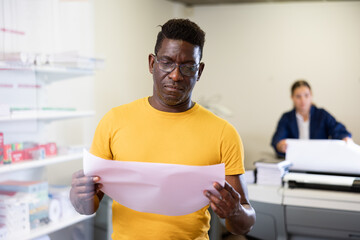 Focused African American male specialist checking the print quality and accepting color proofs in...
