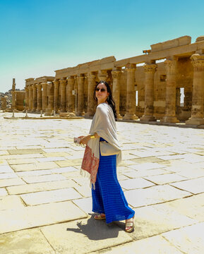 Woman in a blue dress with a white scarf holding a hat at the Philae Temple in Egypt