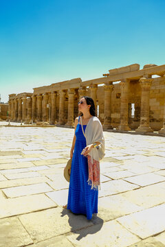 Woman in a blue dress with a white scarf holding a hat at the Philae Temple in Egypt