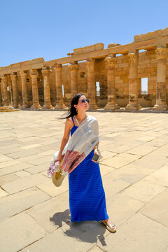 Woman in a blue dress with a white scarf holding a hat at the Philae Temple in Egypt